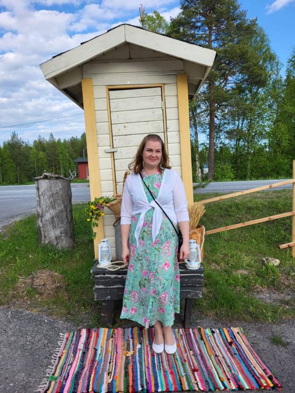 Yrittäjänainen maitolaiturin edessä Käylän Korpihovilla lavatansseissa kukkamekossa